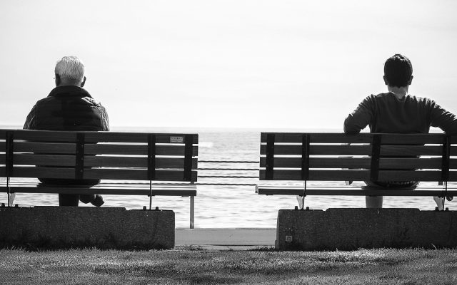 Zwei Bänke mit jeweils einem Mann mit Blick aufs Meer in schwarz weiß